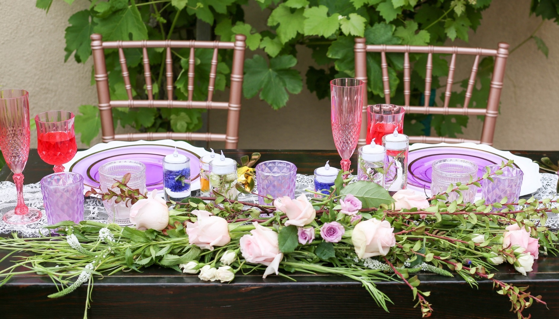 sweetheart table for a wildflower fields wedding features greenery and sprays of flowers with stunning hot pink wine and champagne glasses, and clear lilac colored place settings with gold cutlery.