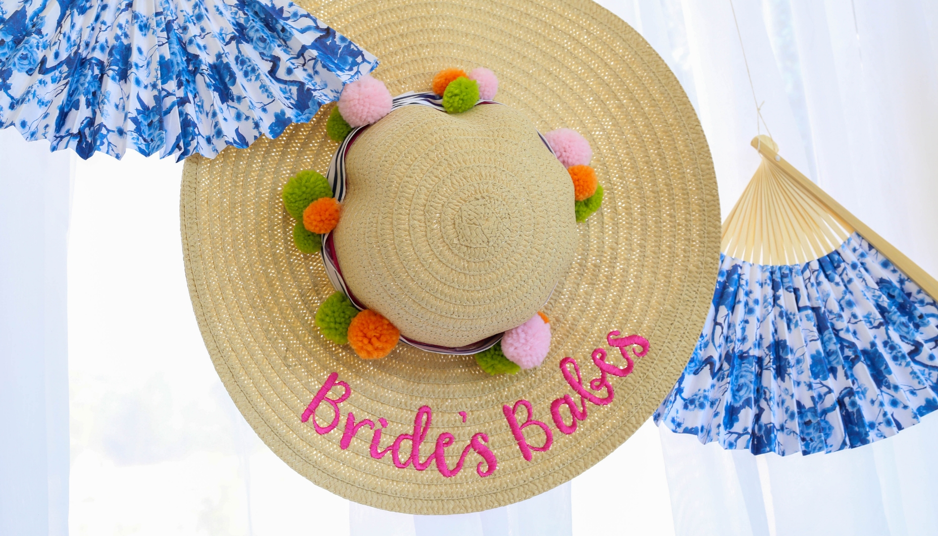 Wide Brimmed Floppy Straw Bridal Party Hats hung on a sheer white curtain backdrop