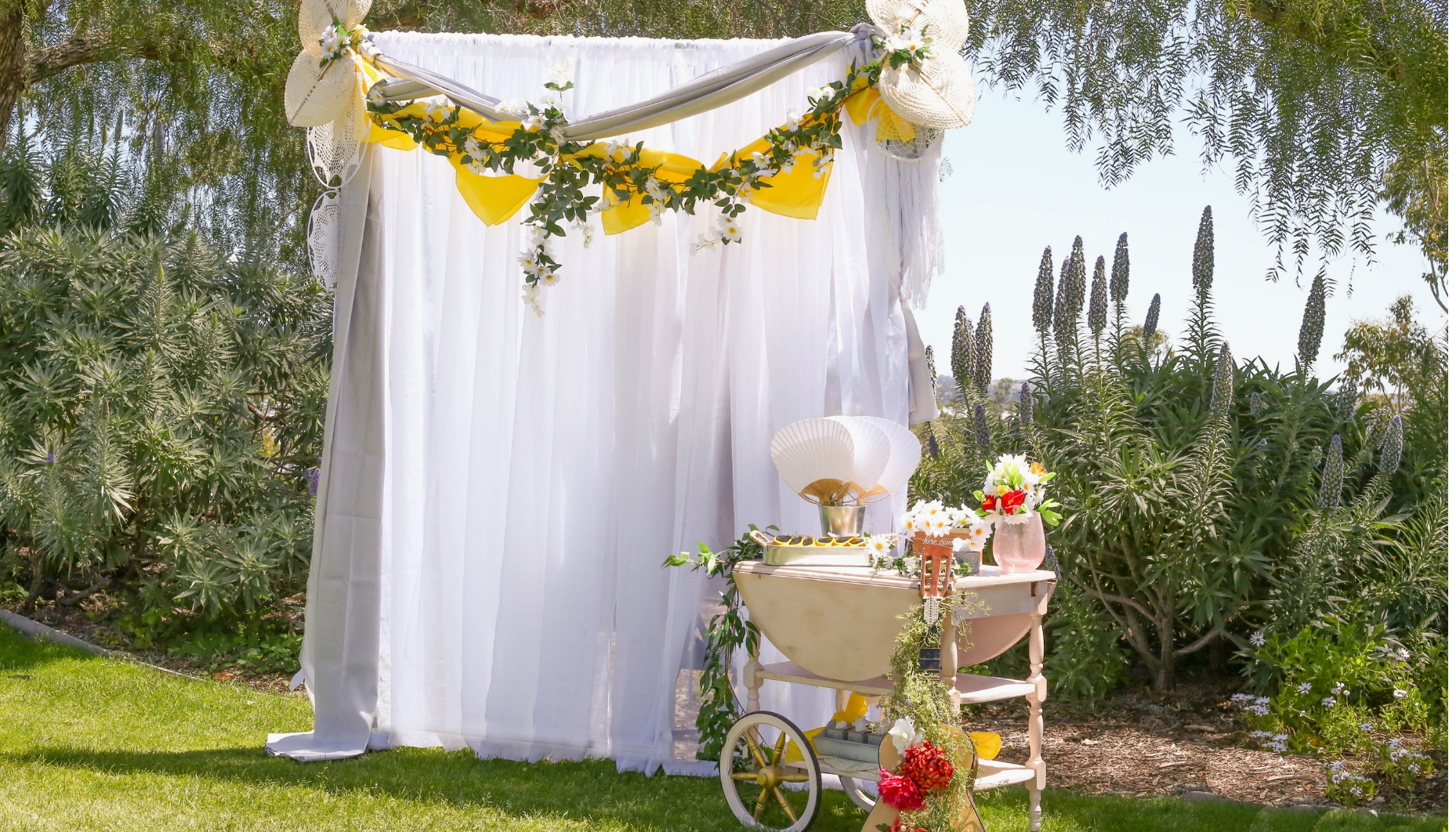 daisy garland drapes across sheer white curtains for a bohemian styled wedding backdrop Bohemian Daisy themed wedding backdrop and ceremony greeting table
