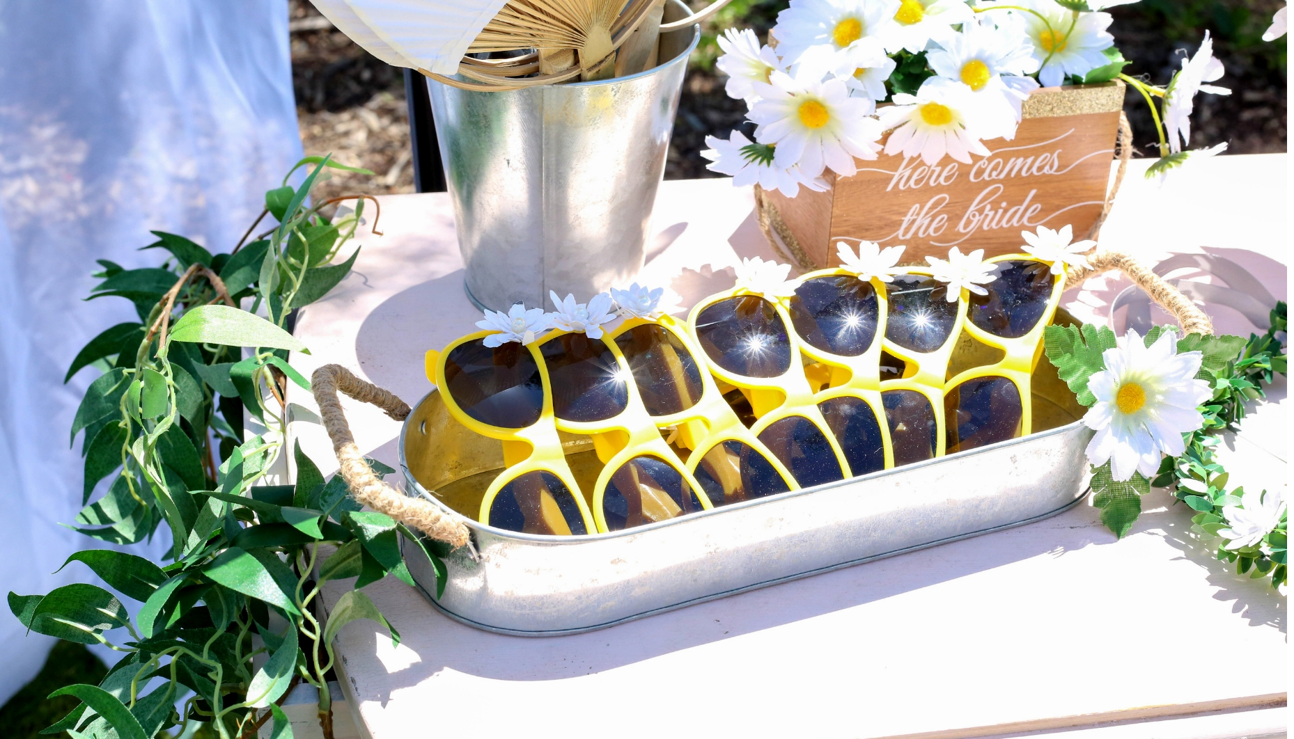 galvanized metal tray with handles holds daisy embellished sunglasses in yellow. Yellow sunglasses are embellished with paper daisies and displayed in a galvanized metal tray with handles.