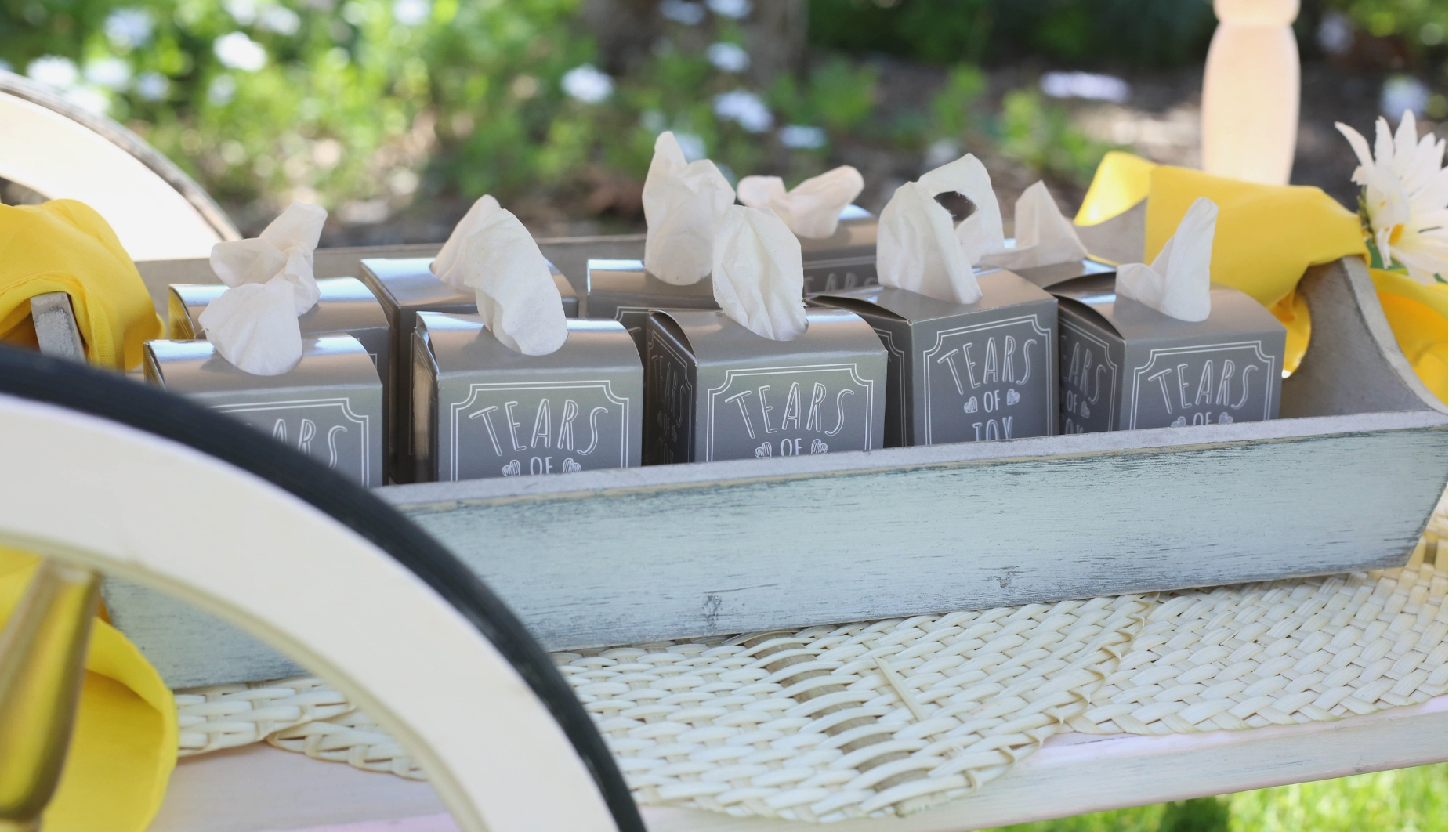 grey weathered tray hold tissues Tears of Joy minature tissue boxes are displayed on a grey weathered tray on the bottom shelf of a vintage pink tea cart.
