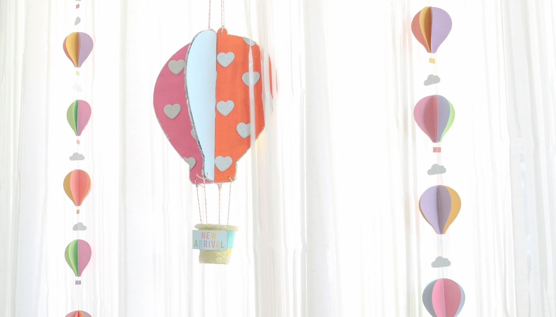 Bright acrylic paint was used to paint the wood hot air balloon decoration which is suspended with string. Colorful paper hot air balloon garlands are hung vertically next to the cute baby shower decor.